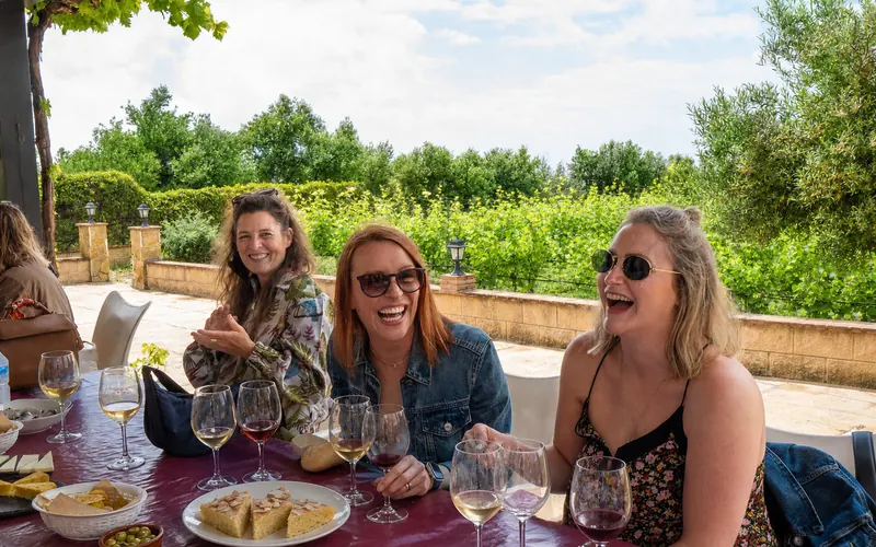 Three guests laughing together over wine and local food at the vineyard
