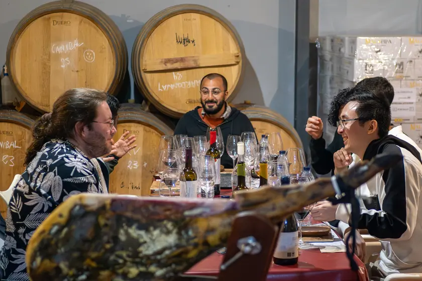 Guests enjoying conversation around a tasting table inside a working wine cellar.