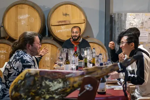 Guests enjoying conversation around a tasting table inside a working wine cellar.