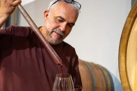 A winemaker drawing red wine from a barrel during a private cellar visit.
