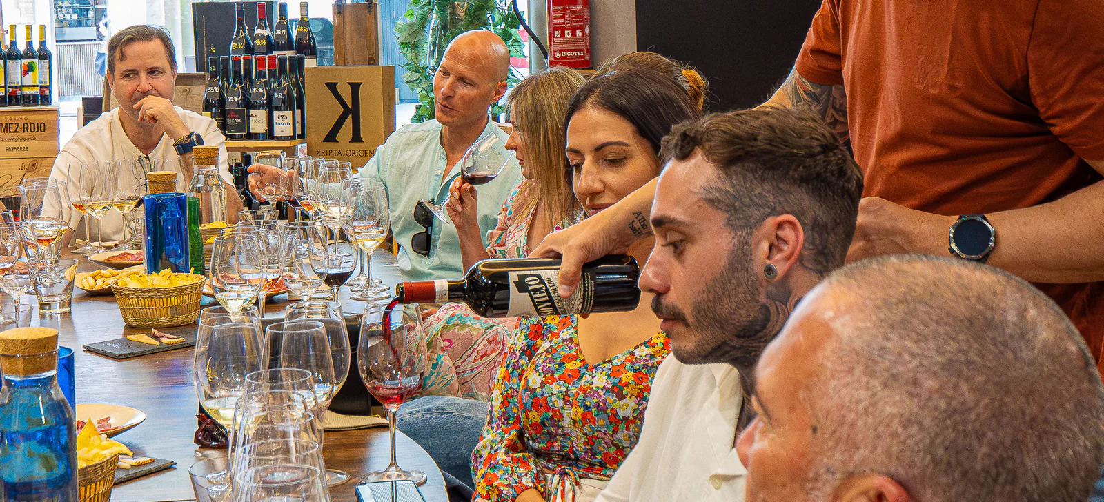 Guests around the shared table while the host pours wine during the tasting.