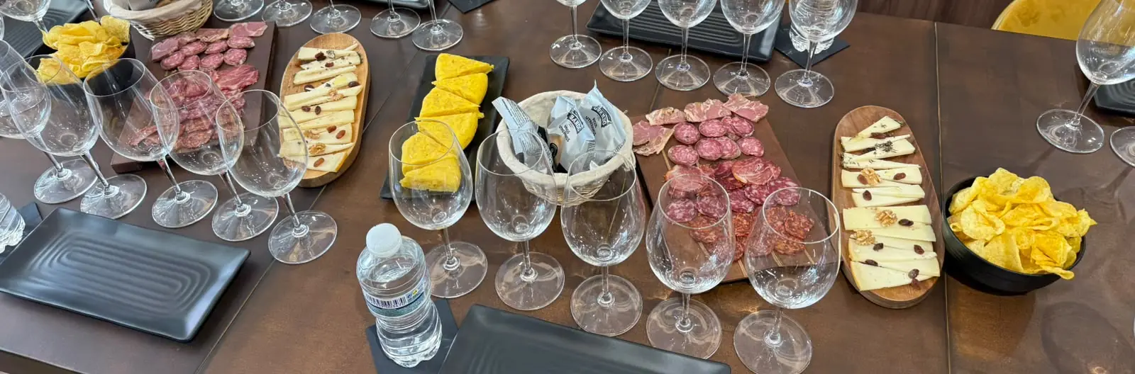 Tasting table prepared with wine glasses, cheeses, cured meats and individual place settings in central Málaga.