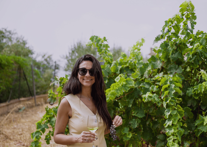 Woman holding a glass of white wine and a bunch of grapes in a sunny vineyard in Malaga